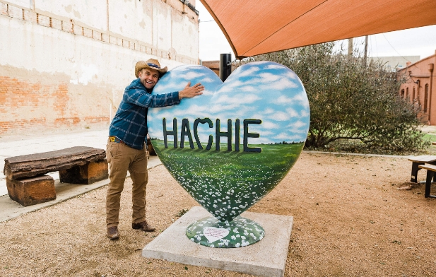 A photograph of Chet Garner "the Daytripper" visiting Waxahachie and hugging a heart with  the name of the town